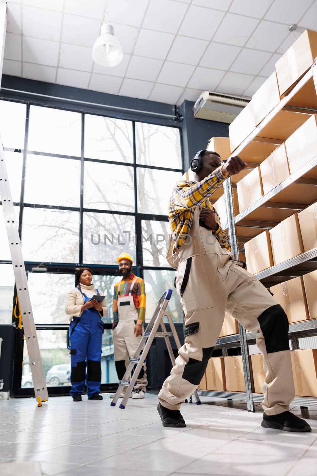 African american young warehouse worker dancing in headphones while doing retail goods inventory. Happy industrial storehouse employee enjoying music and having fun at work