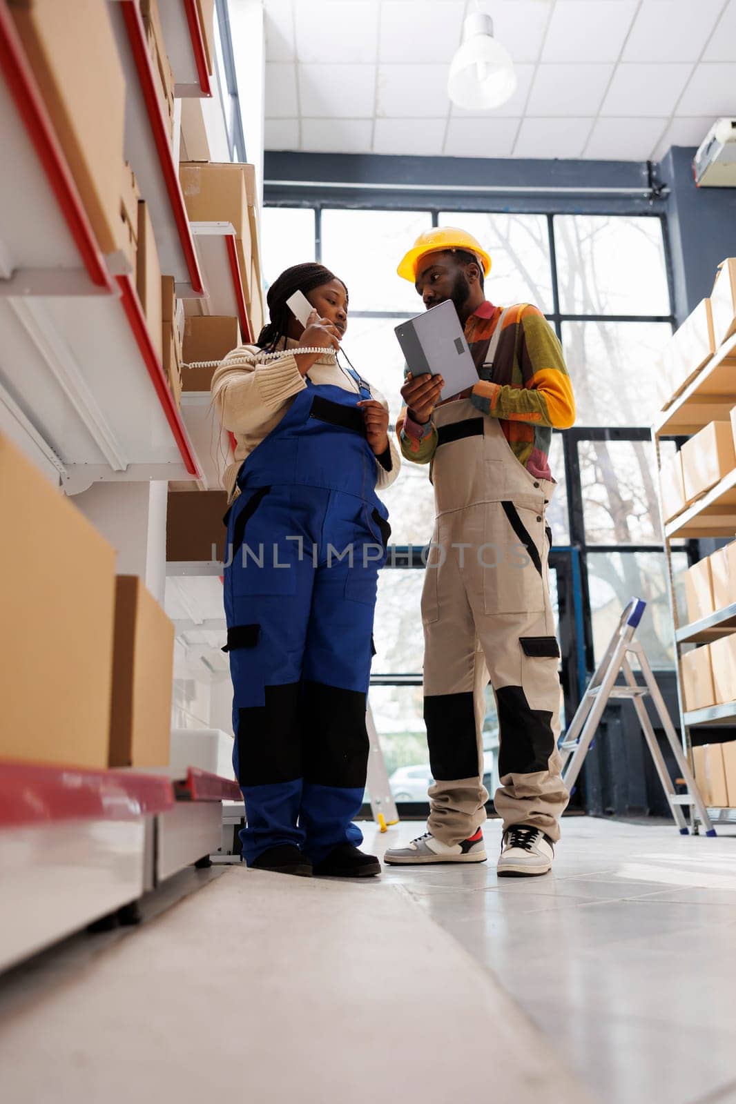 Warehouse operators checking inventory and talking on phone with logistics manager. African american factory storehouse workers speaking with freight distribution department on landline telephone