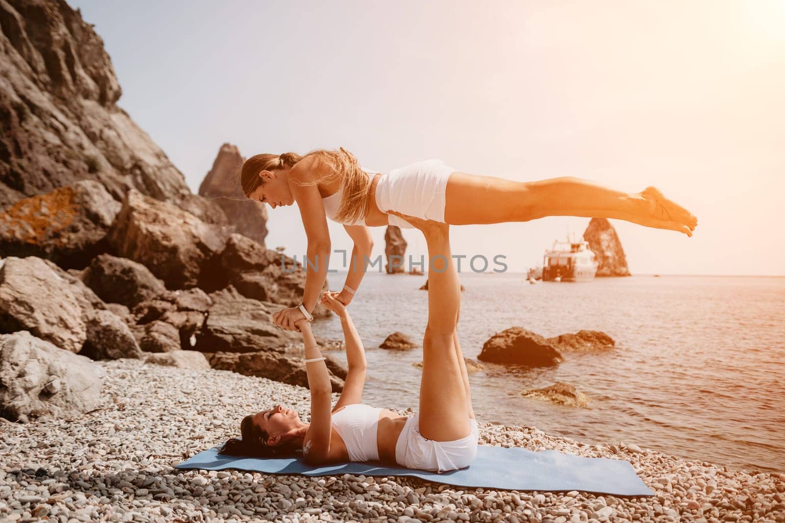 Woman sea yoga. Two happy women practicing yoga on the beach with ocean and rock mountains. Motivation and inspirational fit and exercising. Healthy lifestyle outdoors in nature, fitness concept. by panophotograph