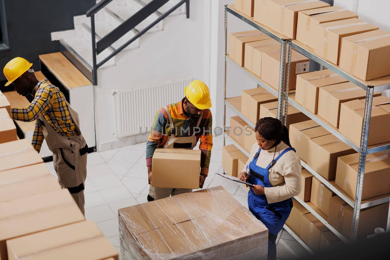 Afrian american package handlers packing parcel and checking order before delivery. All black warehouse loaders and manager team preparing cardboard box for transportation top view