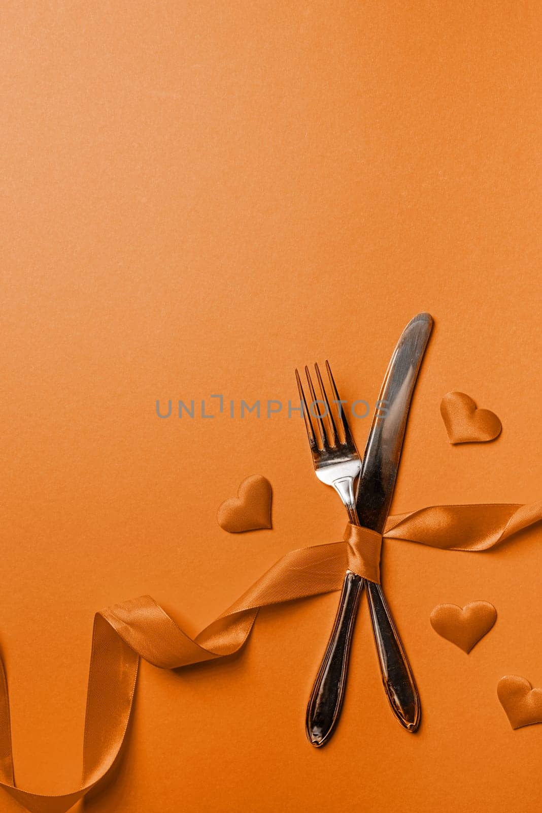 Color of the year 2024: Peach Fuzz. Valentine's Day, romance concept. Fork and knife tied with a red ribbon in a shape of heart rate