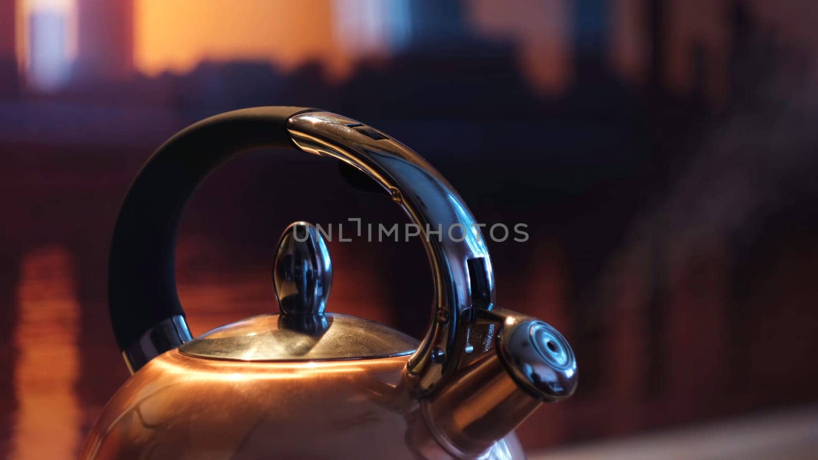 Polished kettle boiling on a gas stove in the kitchen in the evening. Close up of boiling kettle with the steam coming from metal teapot on gas oven.