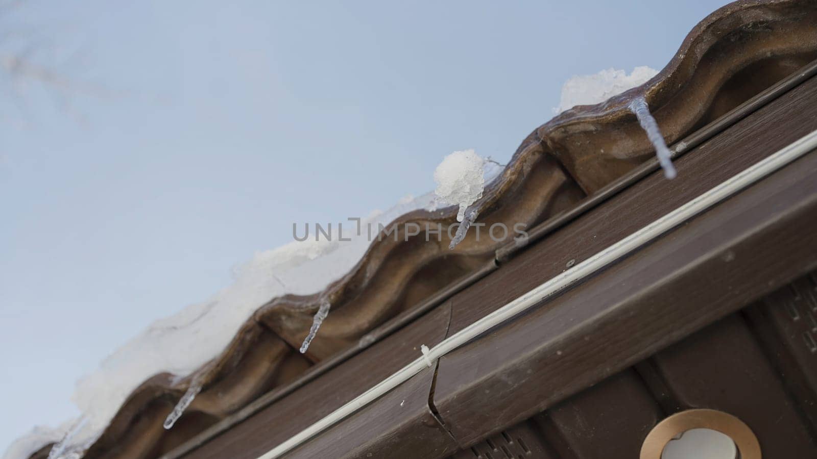 Close-up of dripping icicles on roof of house. Action. Bottom view of dripping icicles from cornice of house. Spring icicles dripping on background of sky.