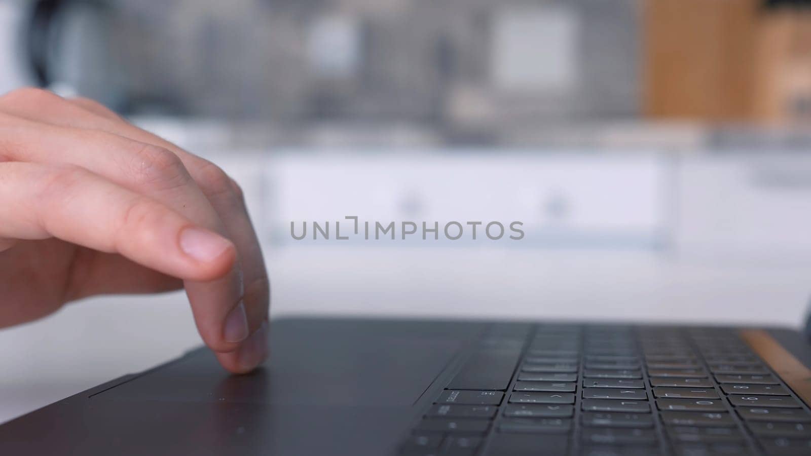 Concept of working at home during isolation. Side view of male hand using touch pad of a new silver laptop that is standing in the kitchen.