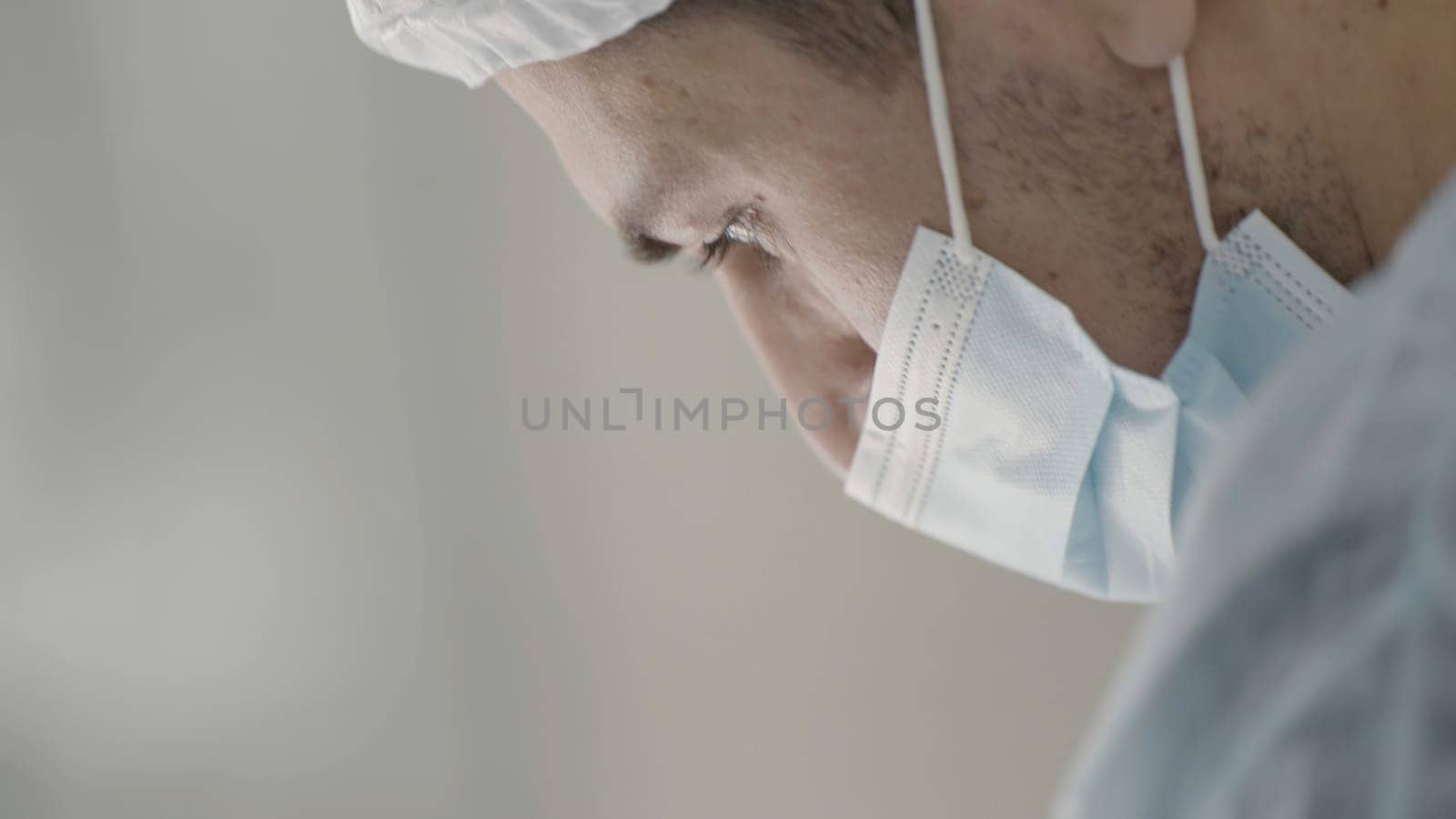 Caucasian male healthcare professional in a hospital operating theatre wearing a surgical cap and mask. Action. Surgeon during procedure