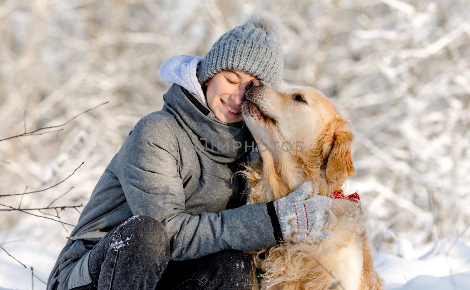 Teenage Girl And Golden Retriever Sit Together In Snow-Covered Forest During Winter