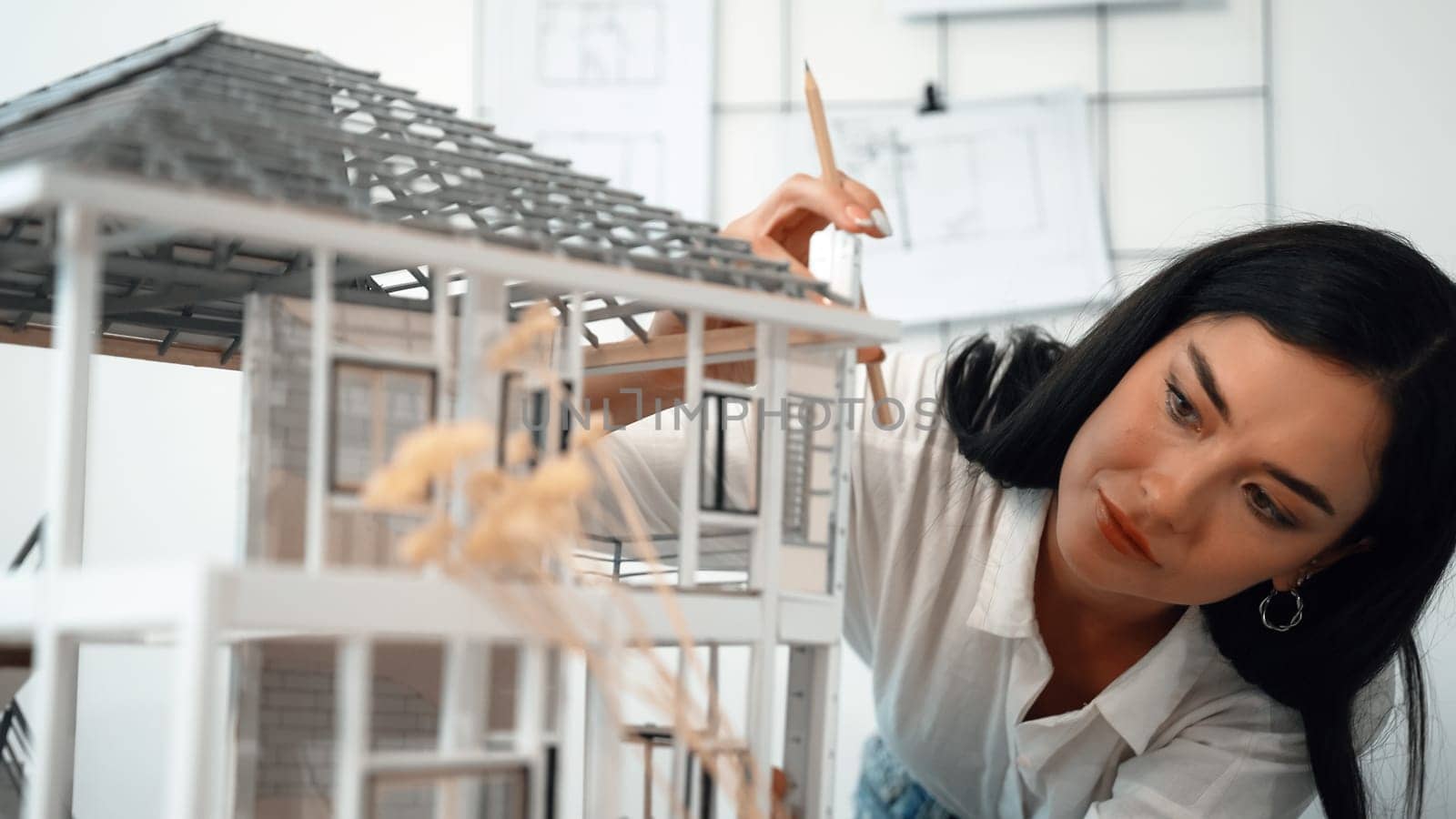 Young beautiful caucasian architect engineer turns house model around to inspect house construction and check mistake point to solve the problem on meeting table at modern office. Closeup. Immaculate.