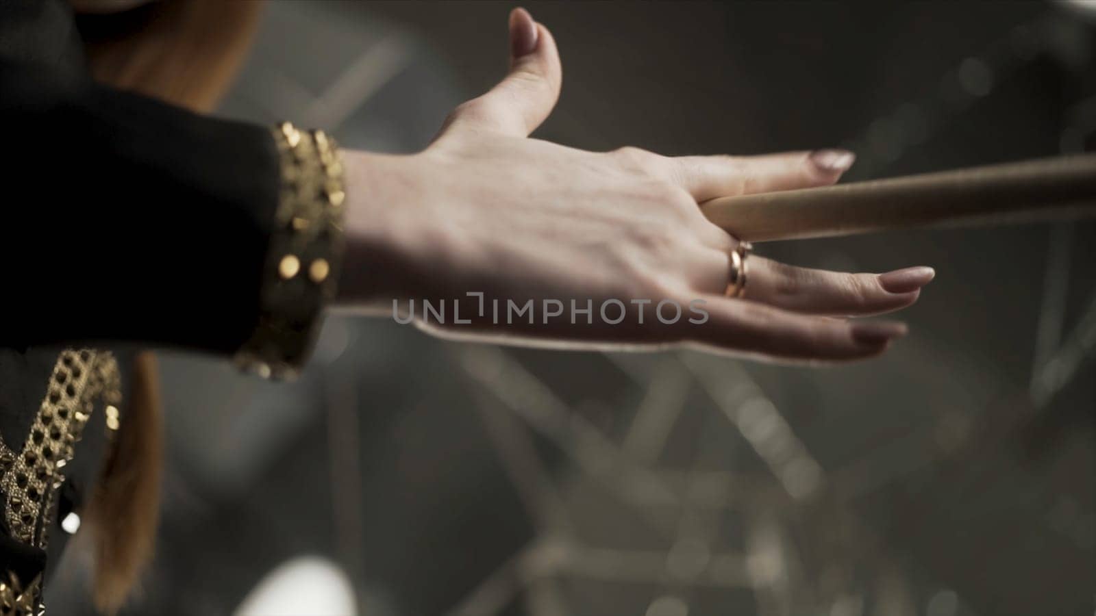 Young attractive woman hand holding drumstick and rotating it during musical rehearsal. Close up for woman hand with manicure and gold rings holding and spinning a drumstick.