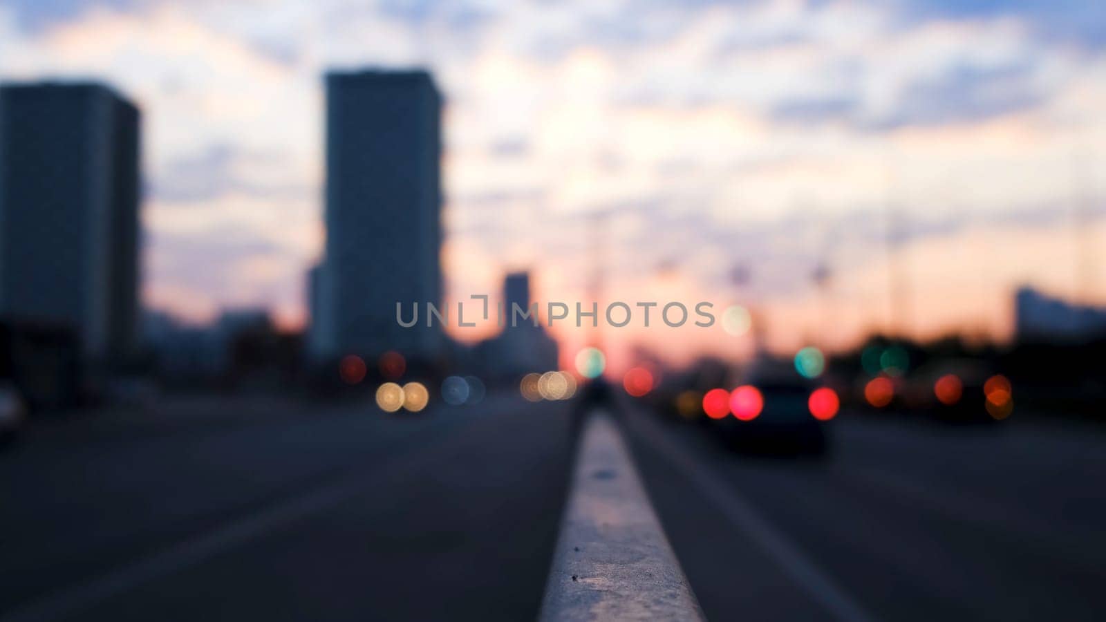 Big city street in the evening with bokeh and blur effect. Sunset sky, high rise buildings and moving cars, urban blurred landscape.