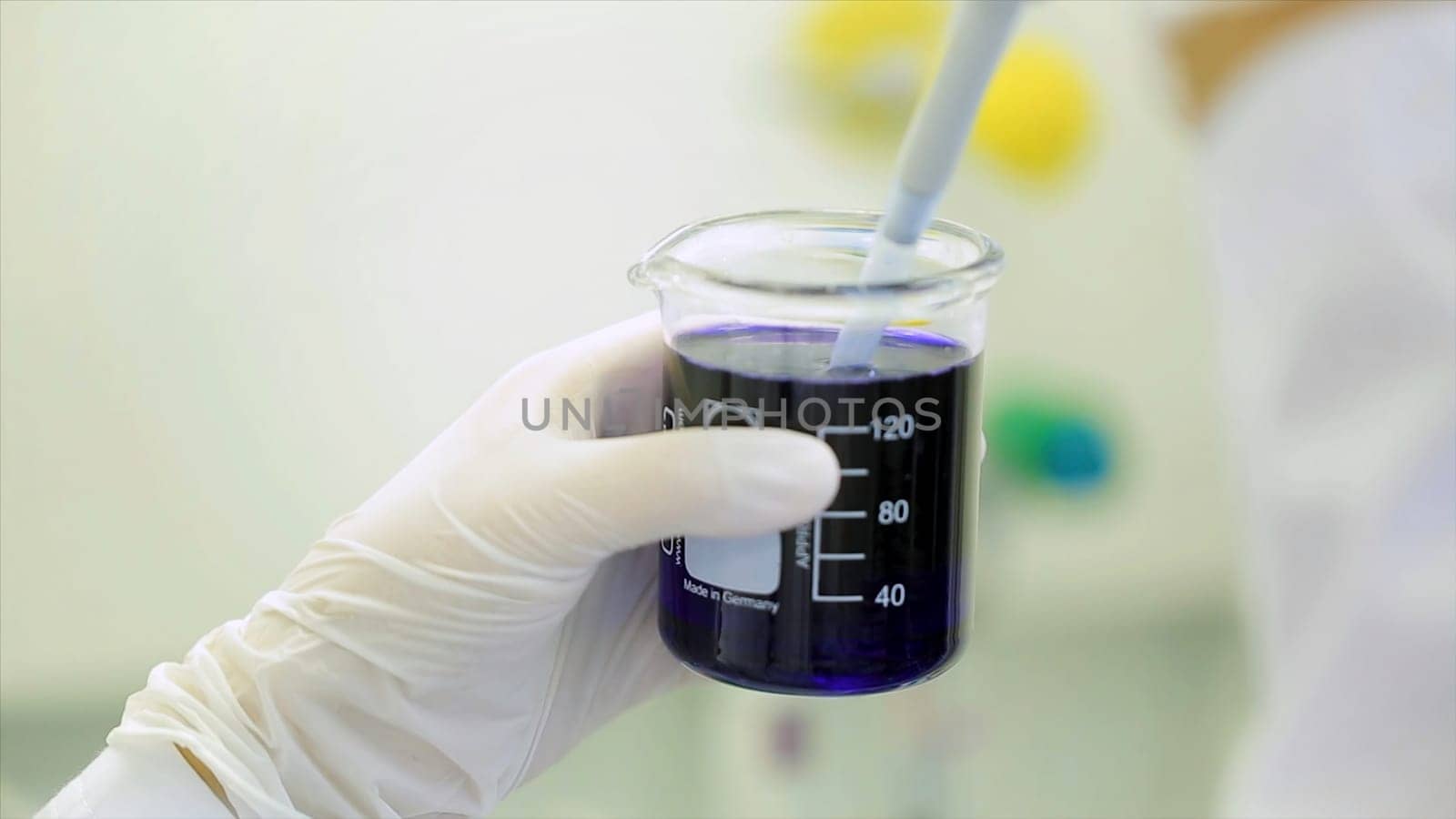 Close-up of glassware with blue fluid in scientist hand during medical test. Hands of clinician holding steel tools during scientific experiment in laboratory. test tubes and dropper.