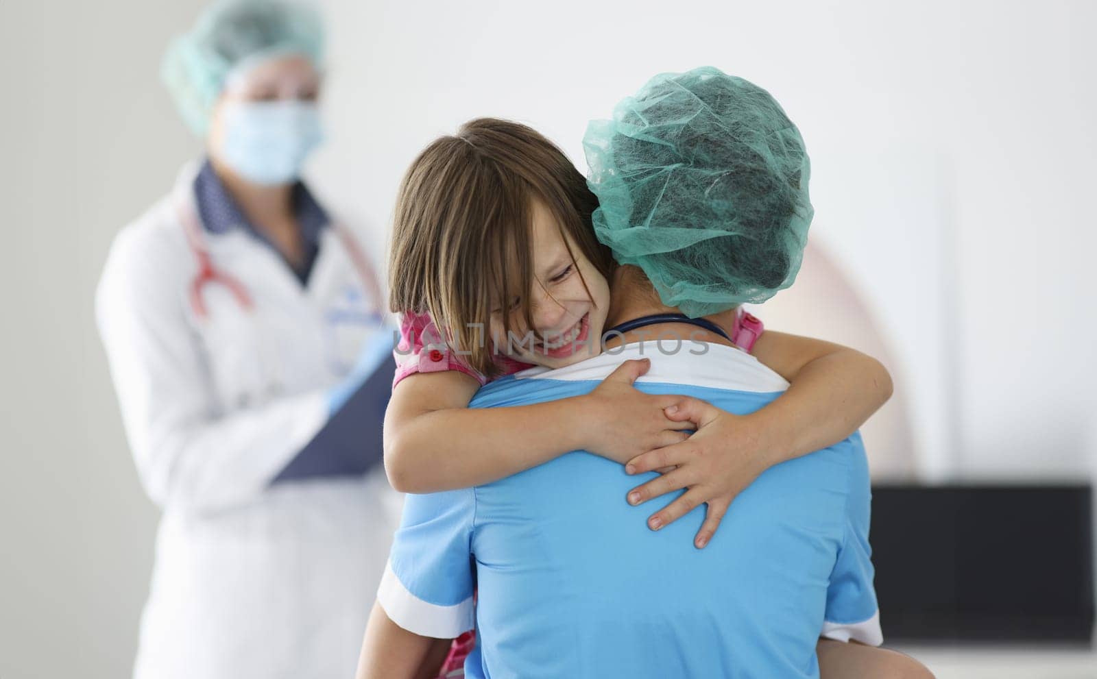 Doctor holds frightened little child girl in arms in clinic. Children fear of injections concept