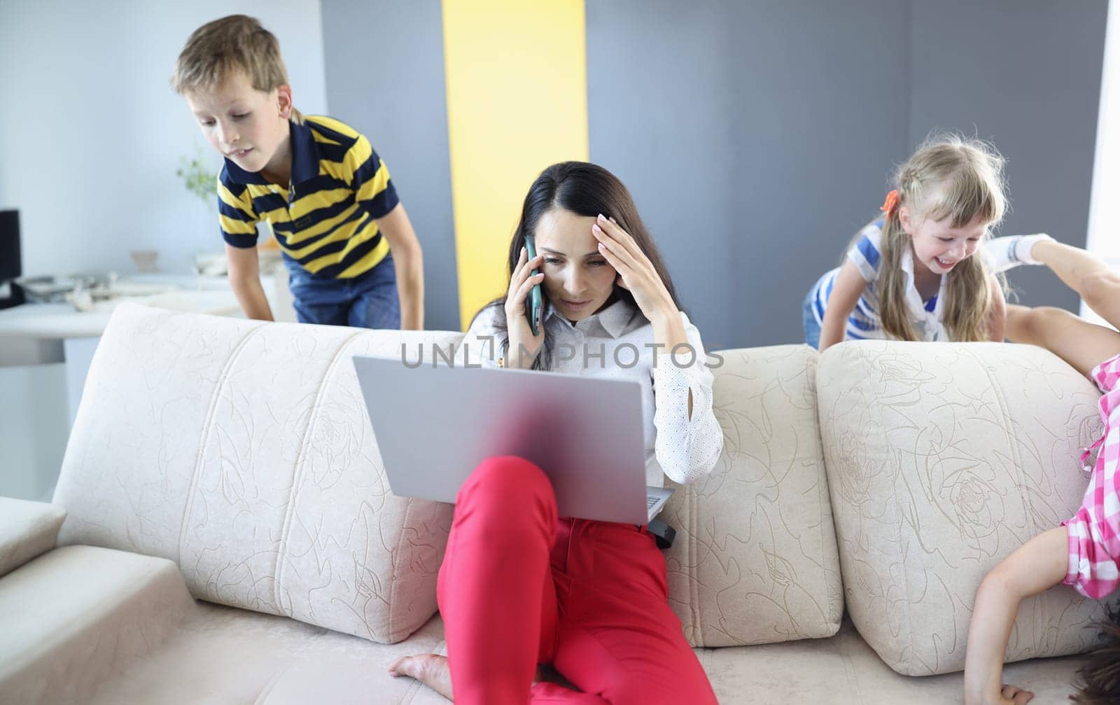 Woman working on laptop at home talking on phone and children playing by kuprevich