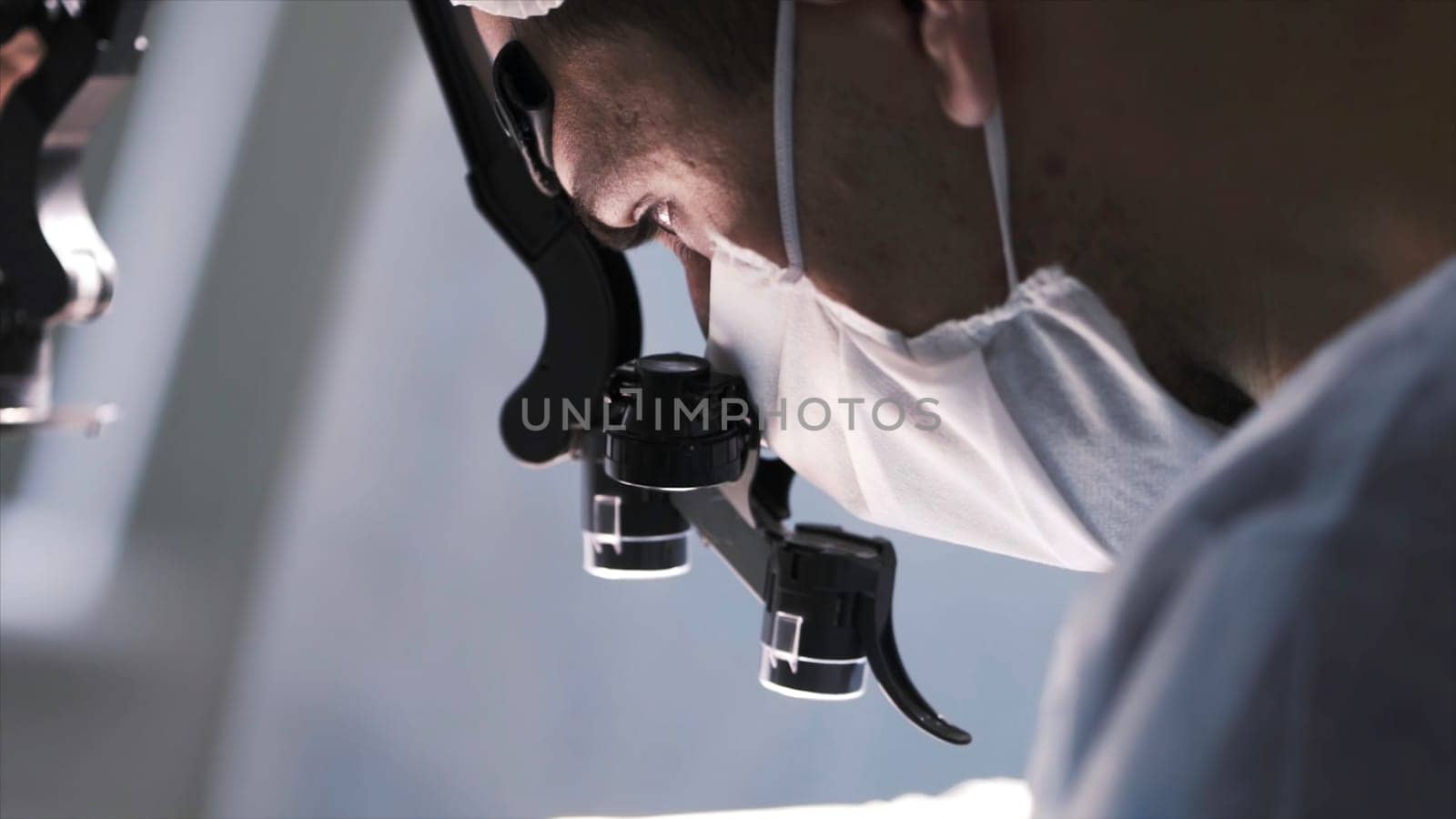 Surgeon head with professional glasses at work. Close up side view of a doctor in glasses with binocular magnifiers examines something at laboratory.