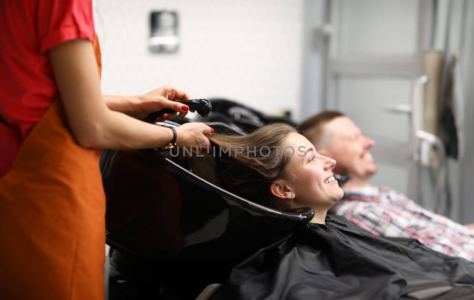 Beautiful happy smiling woman, professional hairdresser washes hair. Charming woman preparing her hair for new haircut concept