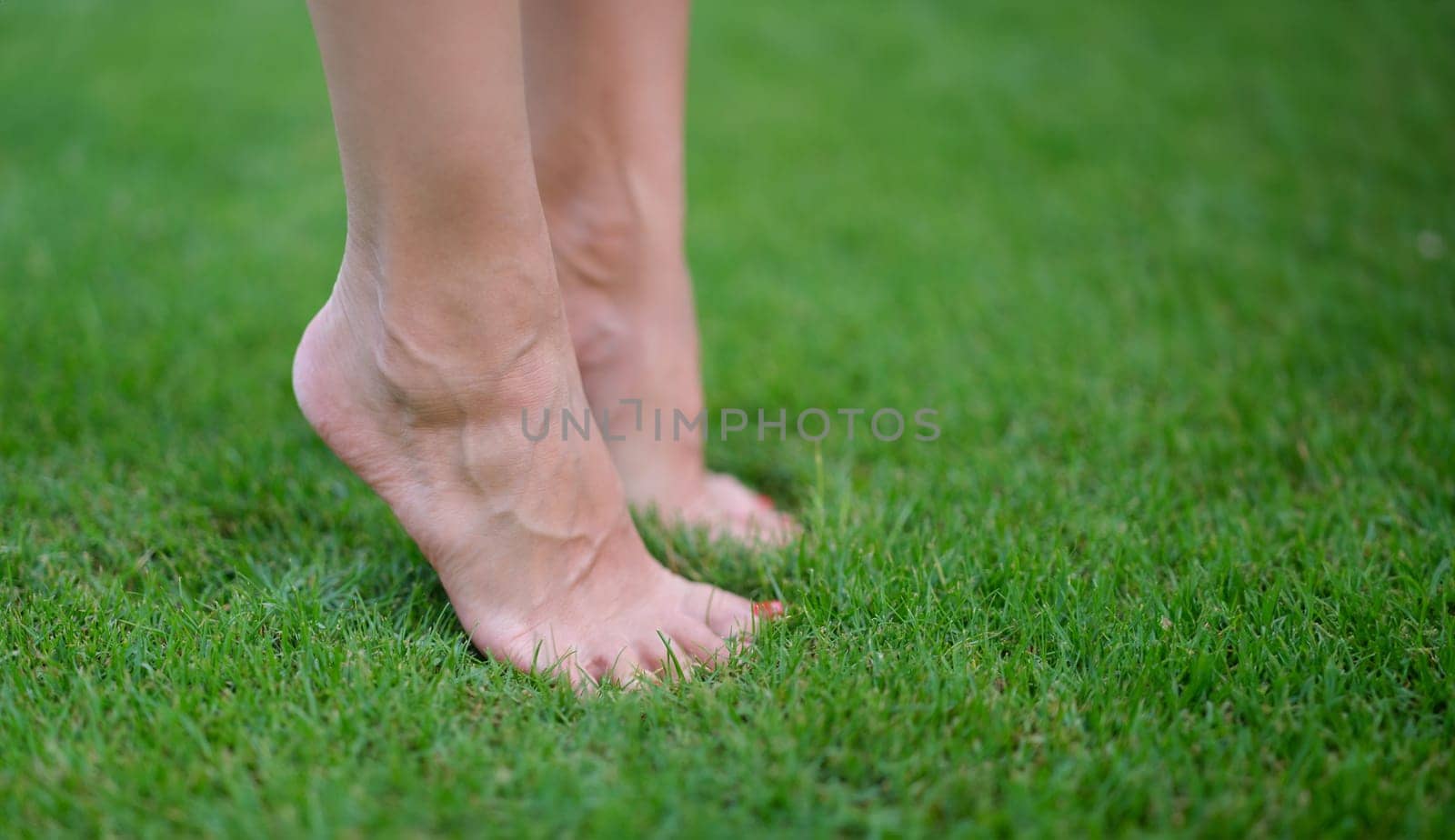 Bare female feet standing on green grass on tiptoe closeup. Yoga in nature concept