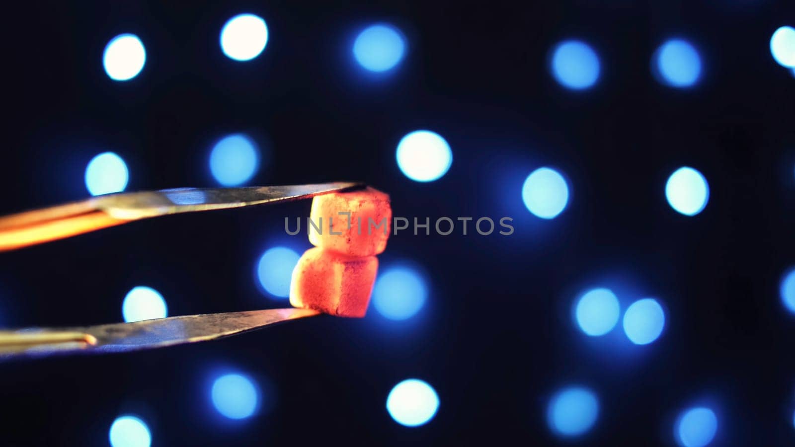 Close up of metal tongs and charcoal for hookah on black background with blue garland. Holding red hot coals with forceps for shisha.