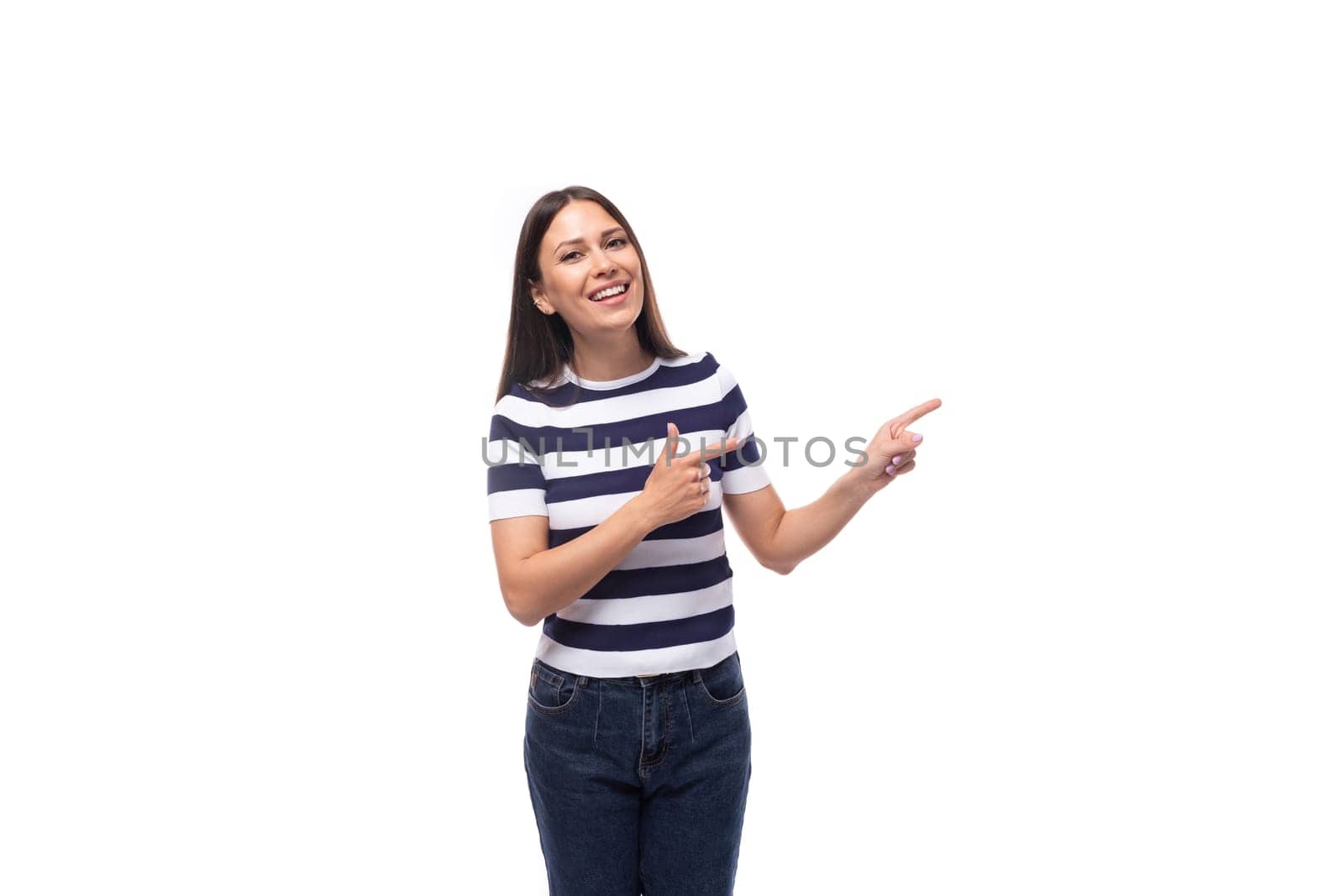 a slender young brunette caucasian woman with light make-up dressed in a striped t-shirt and jeans points with her hands to an empty space by TRMK
