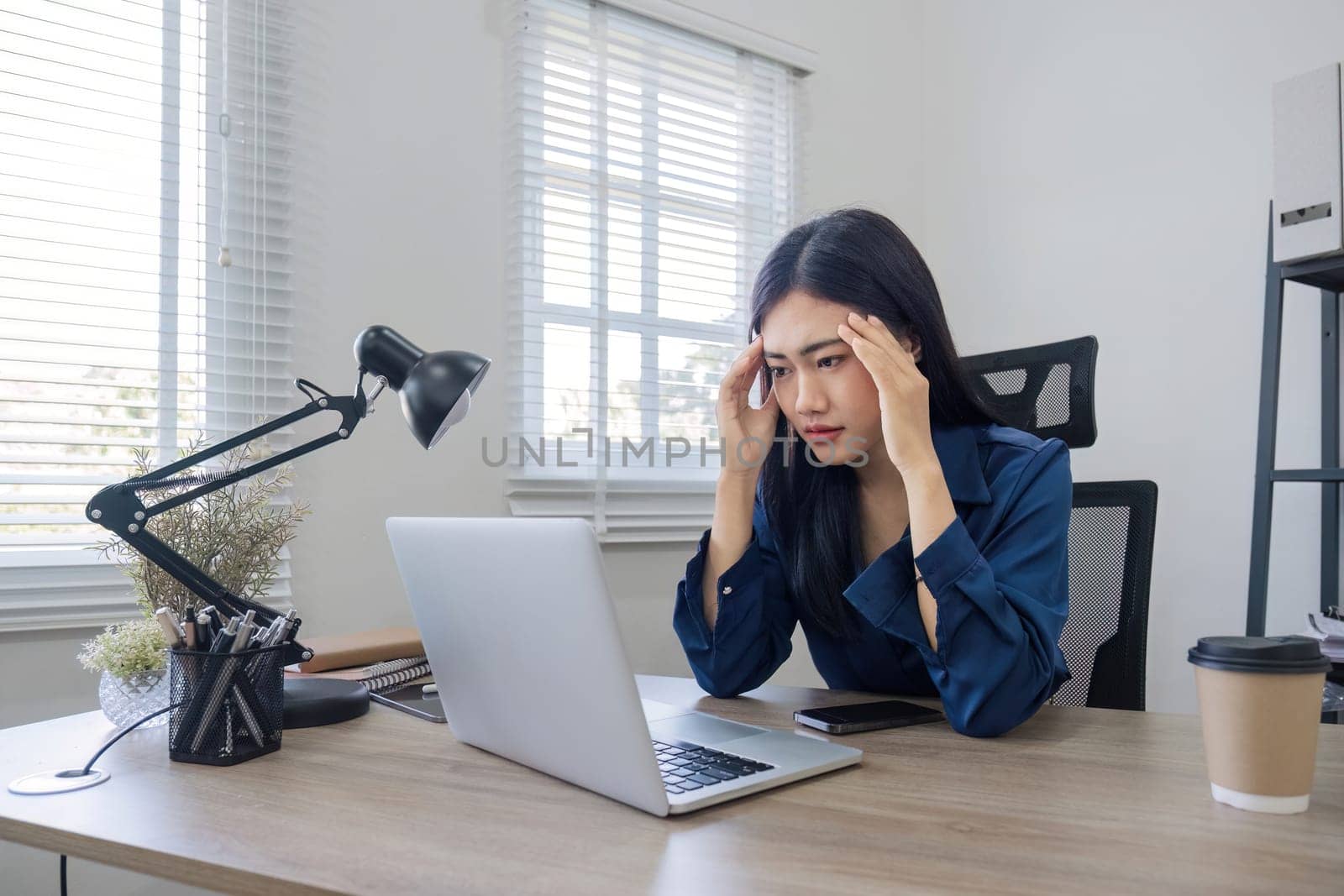 Young Asian business woman is having trouble controlling her online work in front of a laptop screen. Serious Asian businesswoman worried about solving work problems on computer.