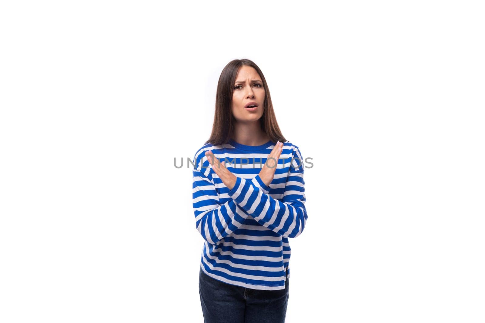 young caucasian woman with dark hair dressed in a blue striped sweatshirt crossed her arms on a white background.