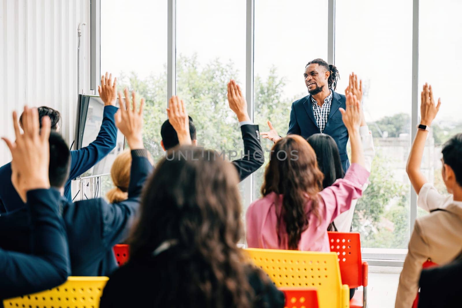 Engaged in a strategy session businesspeople gather in a boardroom for a meeting and seminar. Questions are posed with hands raised by colleagues and employees showcasing teamwork.