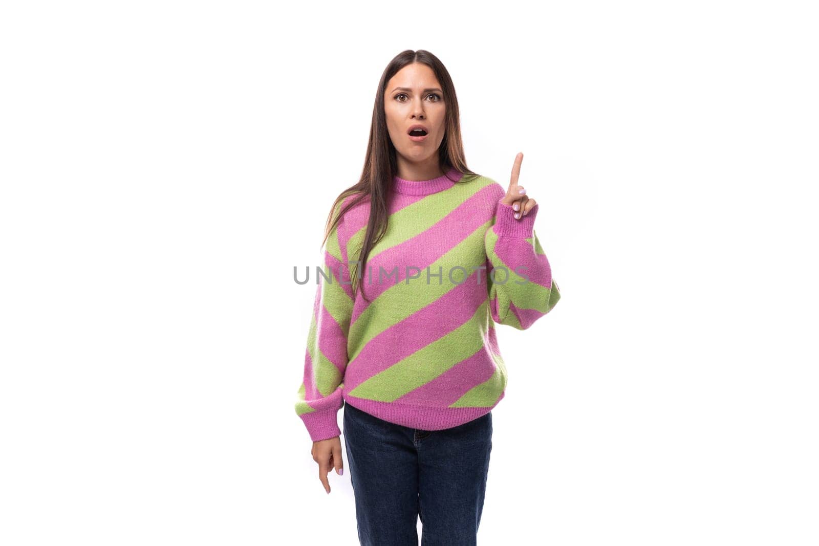 young caucasian woman with straight black hair dressed in a stylish striped pink pullover points with her hand towards an empty space with a place for advertising.