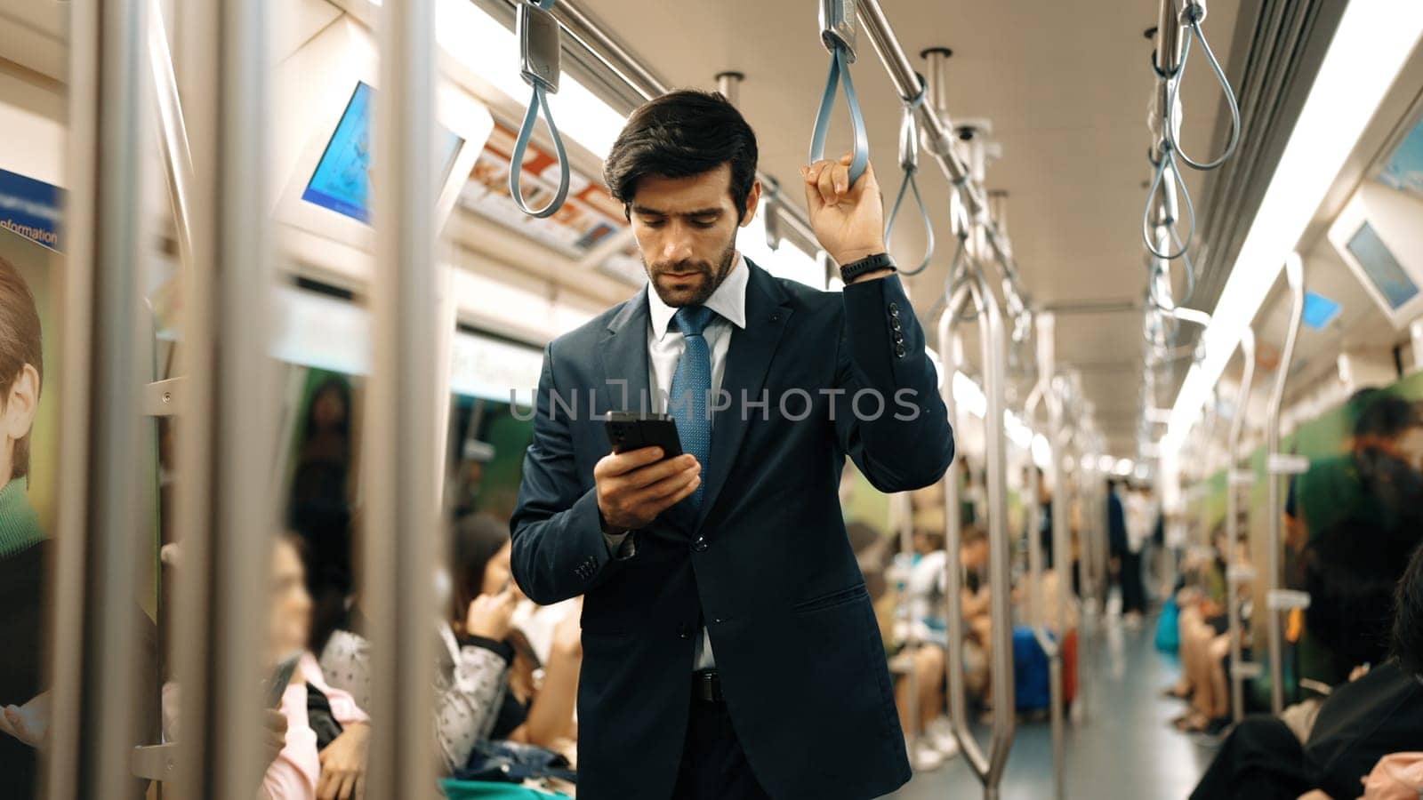 Professional smart business man looking phone while standing at train surrounded by people. Caucasian project manager checking email, planing marketing strategy with blurred background. Exultant.