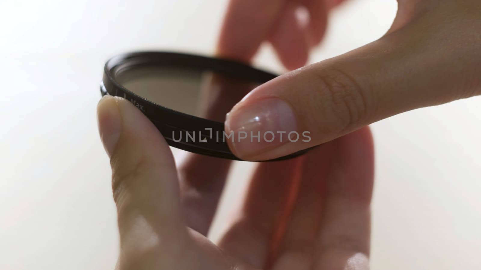 Close up of polarizing lens filter in girls hands isolated on white background. Woman turning into the both sides mechanism of lens filter.