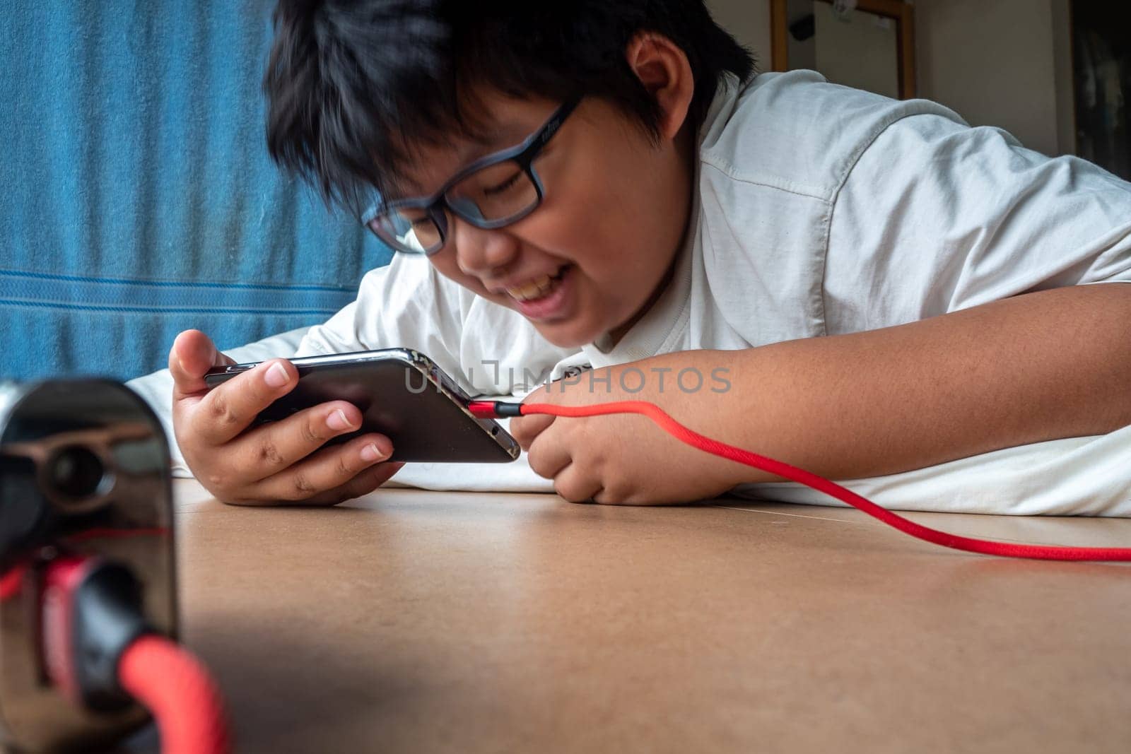 An Asian boy lies prone while seeing media on smartphone by Satakorn