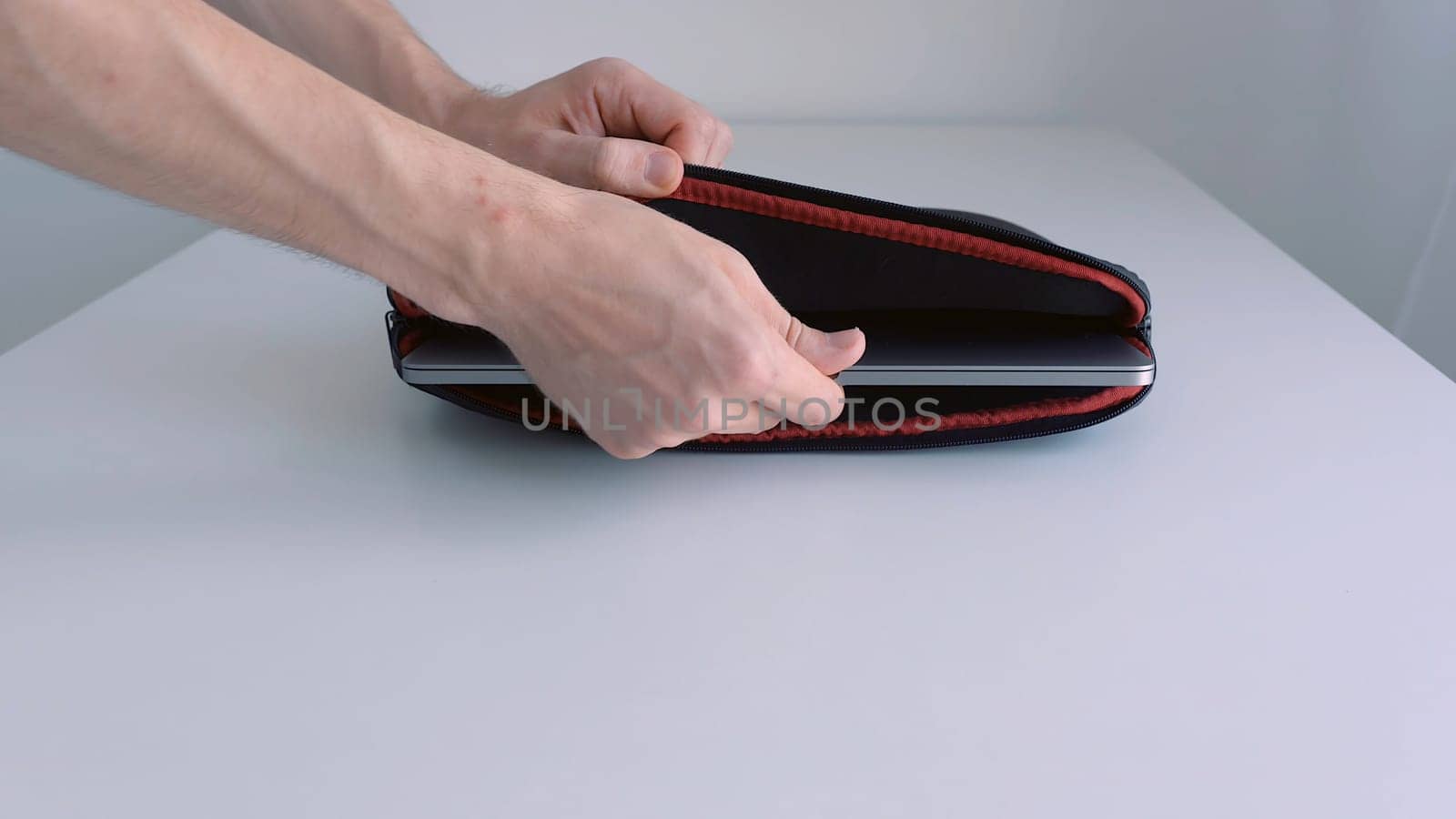 Man hand putting laptop into a case, zipping it up and taking away of the table. Close up of male hand placing modern portable computer into the bage and taking it away.