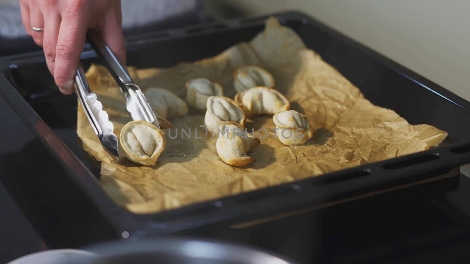 Dumplings baked on a pan. ART. The cook took one dumpling with tongs. Eight baked dumplings lie on a baking sheet and paper.