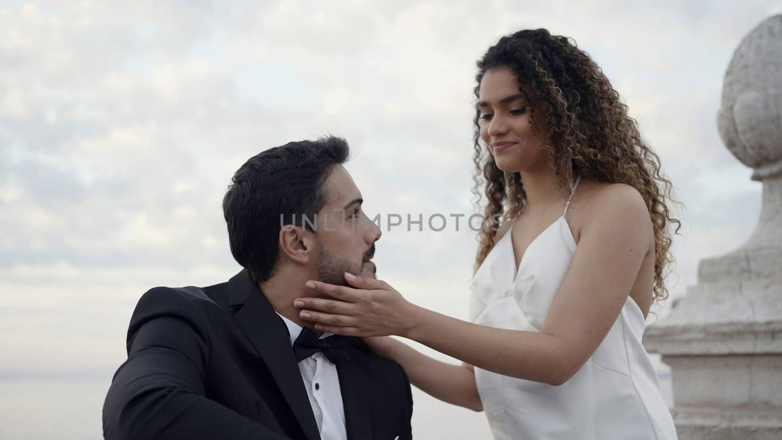 Happy couple in suit and white dress on a date outdoors. Action. Woman with curly hair gently touching face of a man in official suit