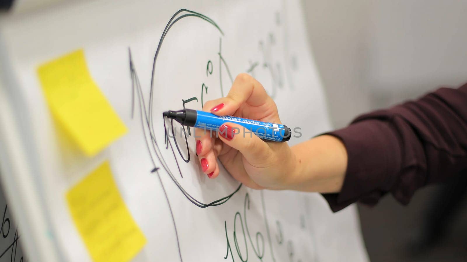 Businessman putting his ideas on white board during a presentation in conference room. Focus in hands with marker pen writing in flipchart. Close up of hand with marker drawing graph on office white board