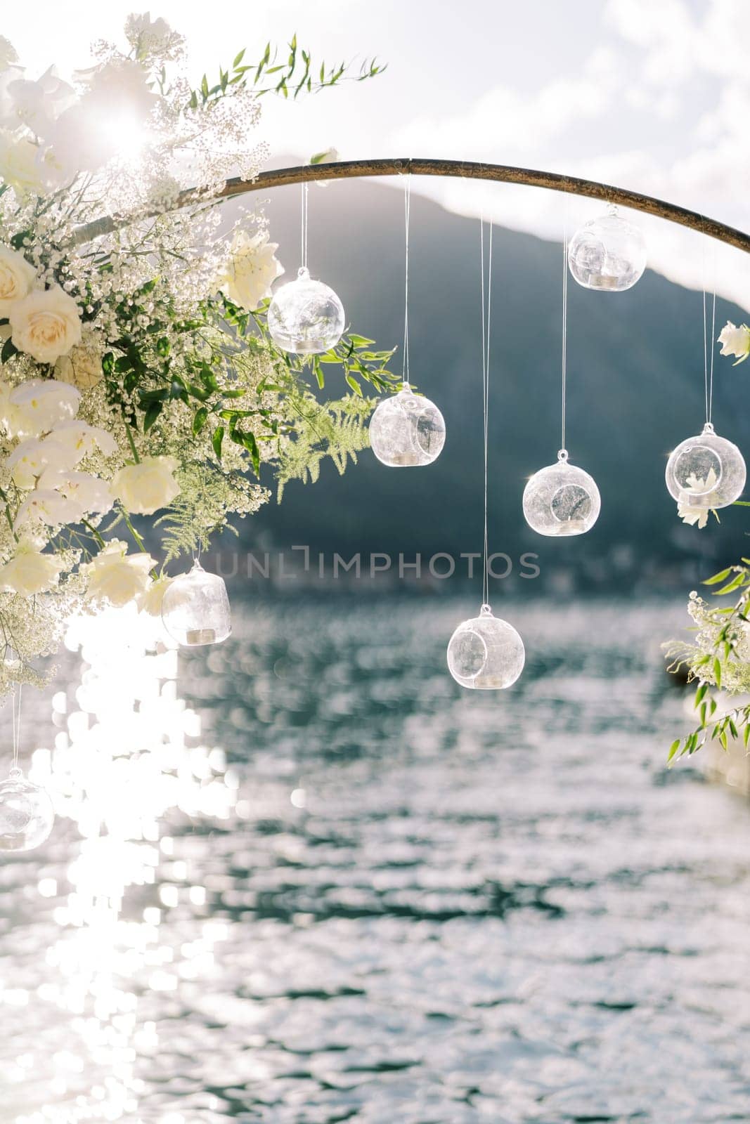Tablet candles in round ball-candlesticks hang from a wedding arch standing by the sea. High quality photo