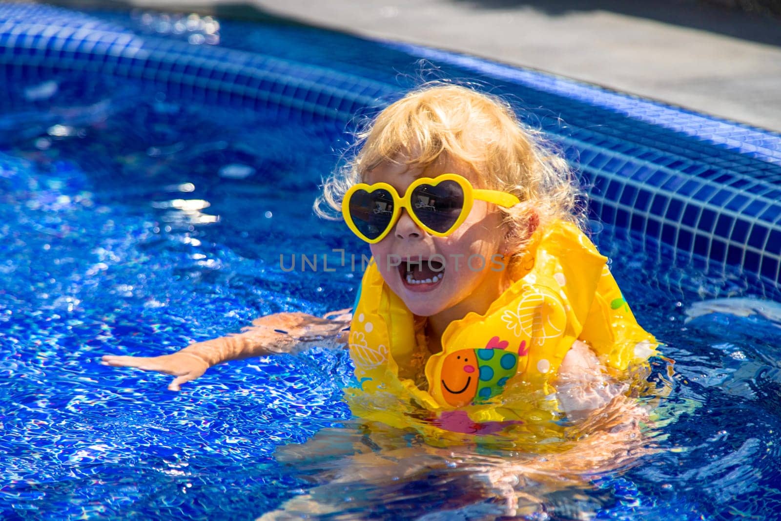A child in a vest swims in the pool. Selective focus. Kid.