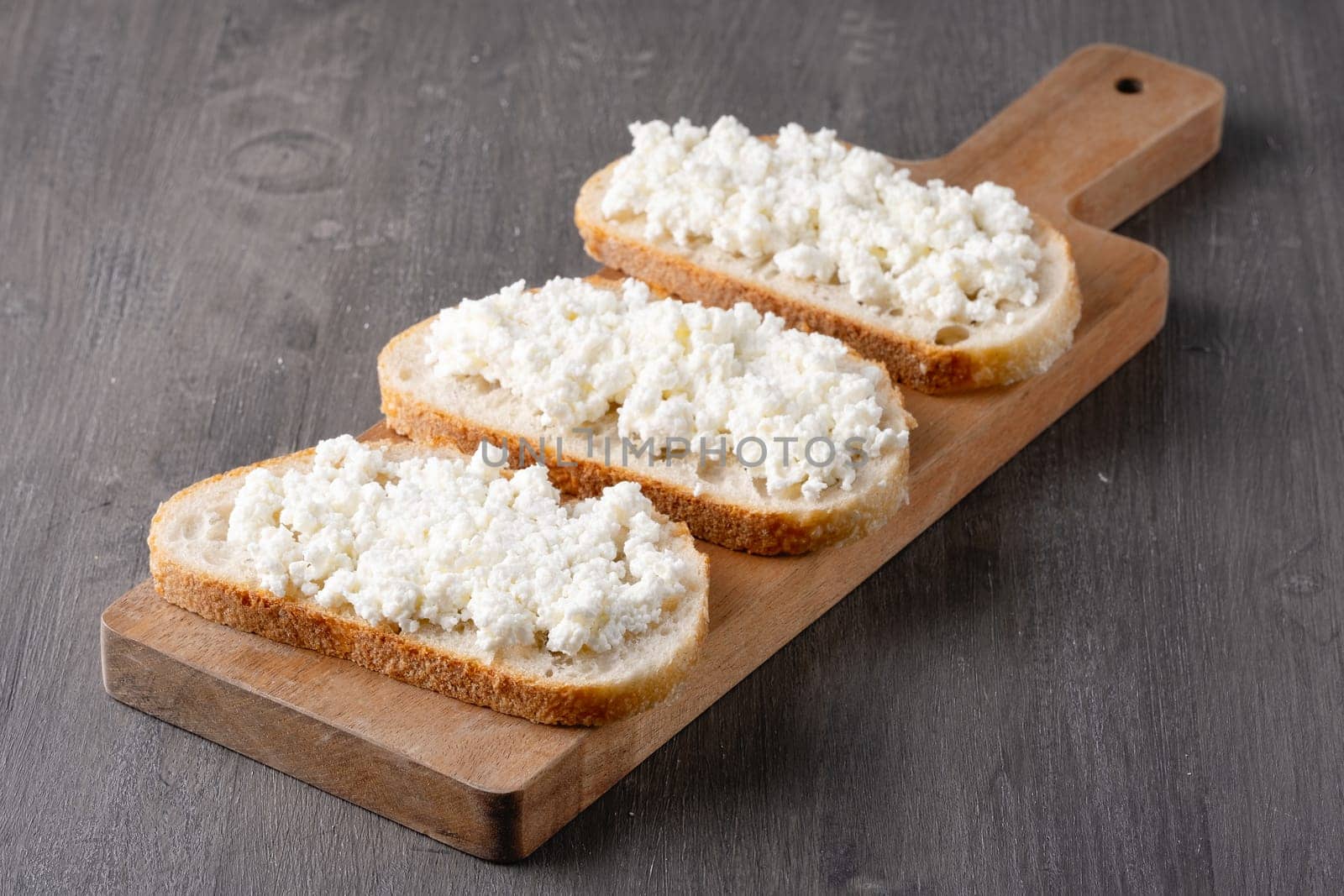 Bread with curd cheese on wooden board.