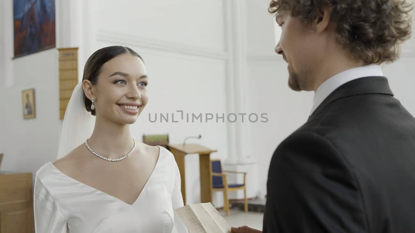 The wedding ceremony. Action.A huge hall with chairs where a young groom in a suit and a bride in a long white dress with a veil are getting married. High quality 4k footage