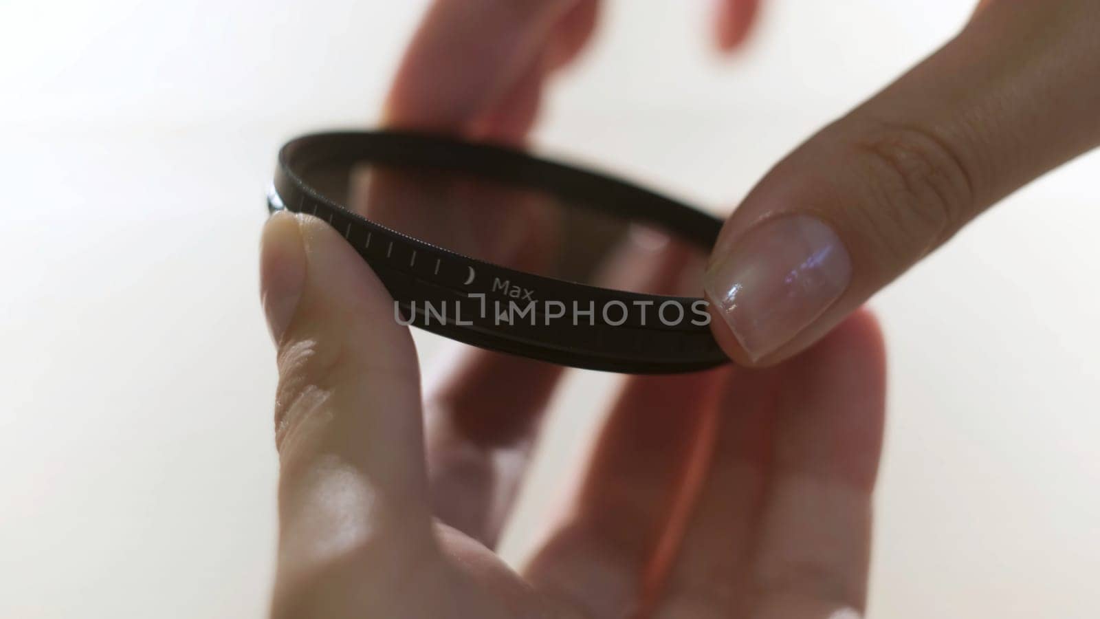 Close up of polarizing lens filter in girls hands isolated on white background. Woman turning into the both sides mechanism of lens filter.