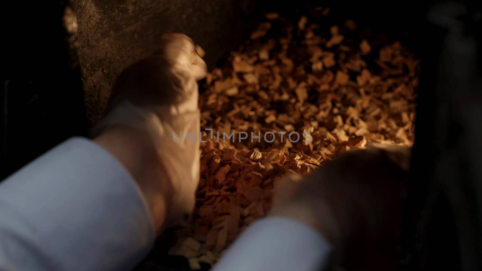 A man puts sawdust in a cast iron furnace close-up. Man's hands putting wood into the fire close up. Wood furnace. Open firebox with a hardwood log laid inside a furnace. Flames and an ember are visible in a blurry background.