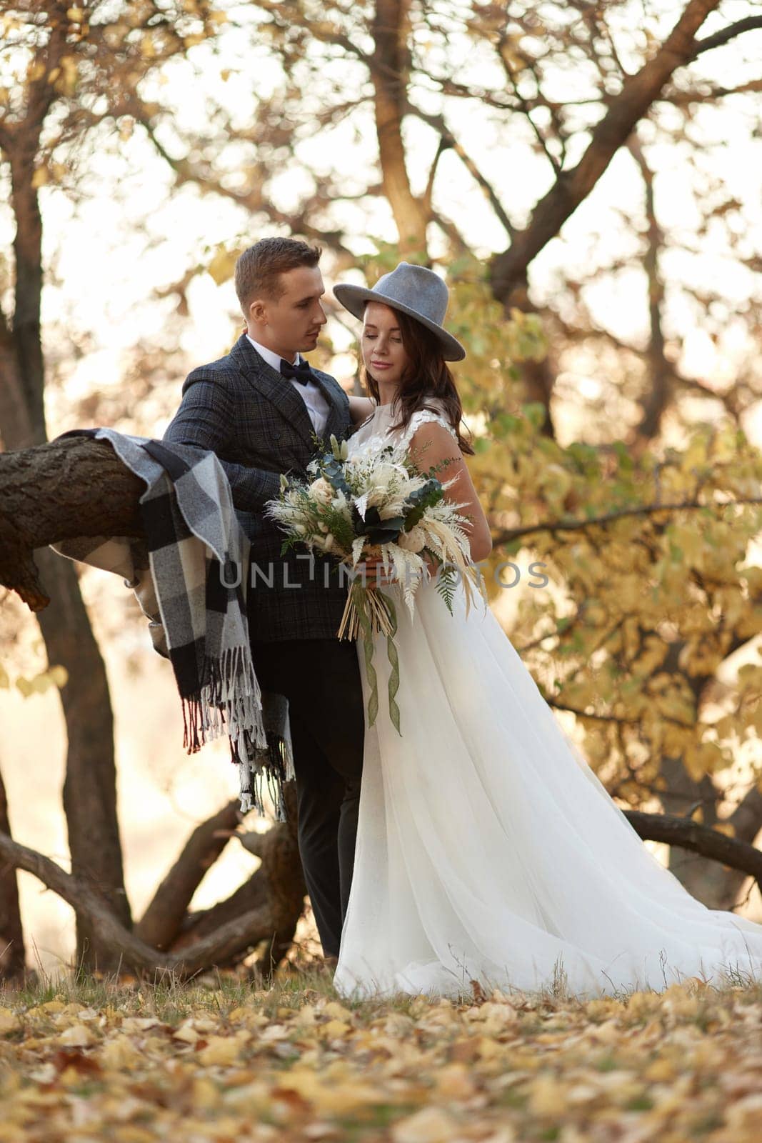 beautiful happy stylish bride in hat and groom standing outdoor in autumn
