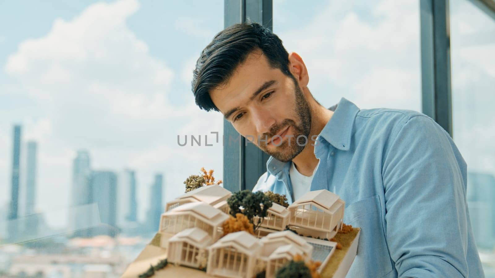 Businessman in casual outfit holding house model while checking house construction. Architect engineer inspect building model while standing near window with skyscraper. Engineering. Tracery