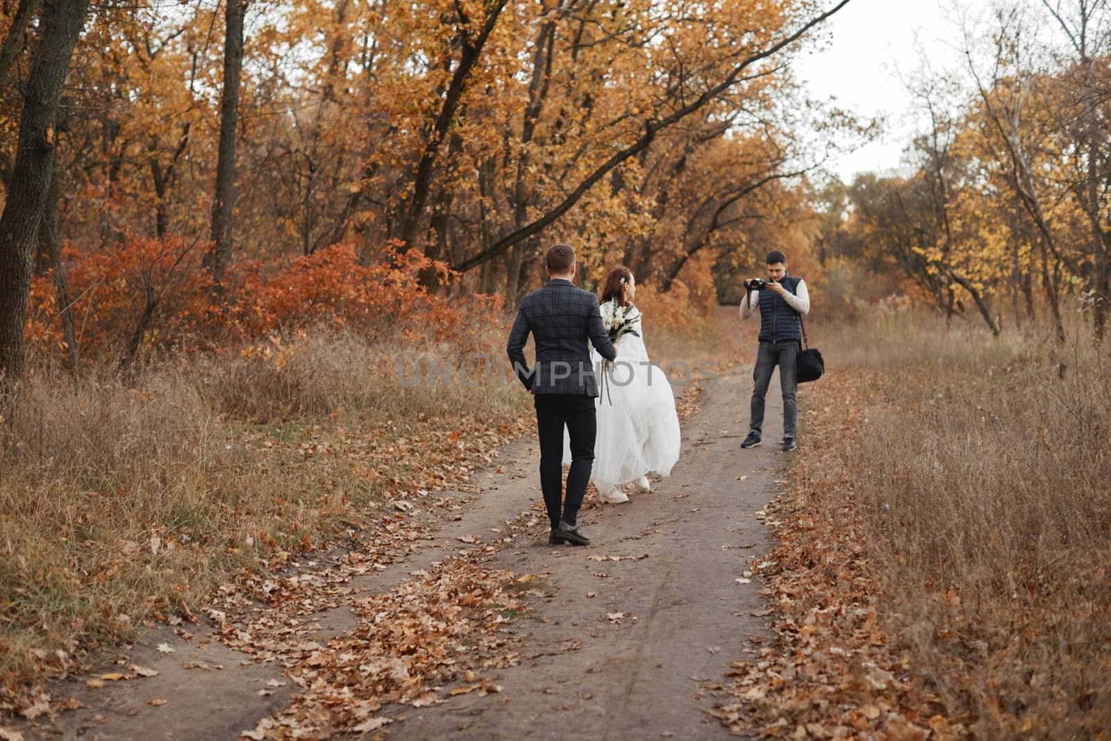 Professional wedding photographer taking pictures of the bride and groom in nature in autumn