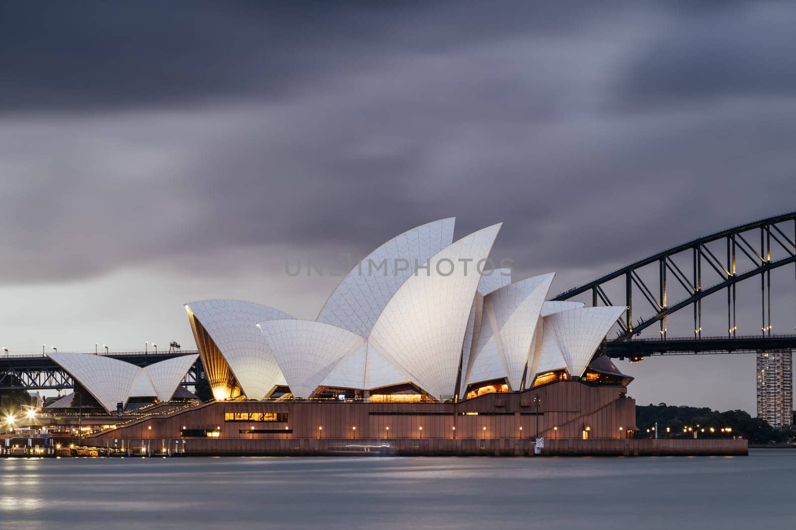 SYDNEY, AUSTRALIA - DECEMBER 03 2023: Sydney Opera House and Harbour Bridge at dusk during a summer storm from Mrs Macquarie's Chair in Sydney, New South Wales, Australia