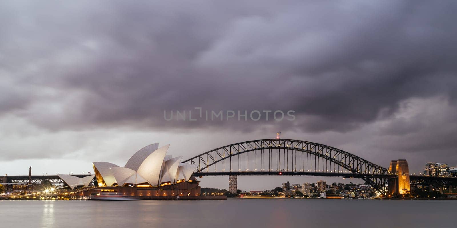 SYDNEY, AUSTRALIA - DECEMBER 03 2023: Sydney Opera House and Harbour Bridge at dusk during a summer storm from Mrs Macquarie's Chair in Sydney, New South Wales, Australia