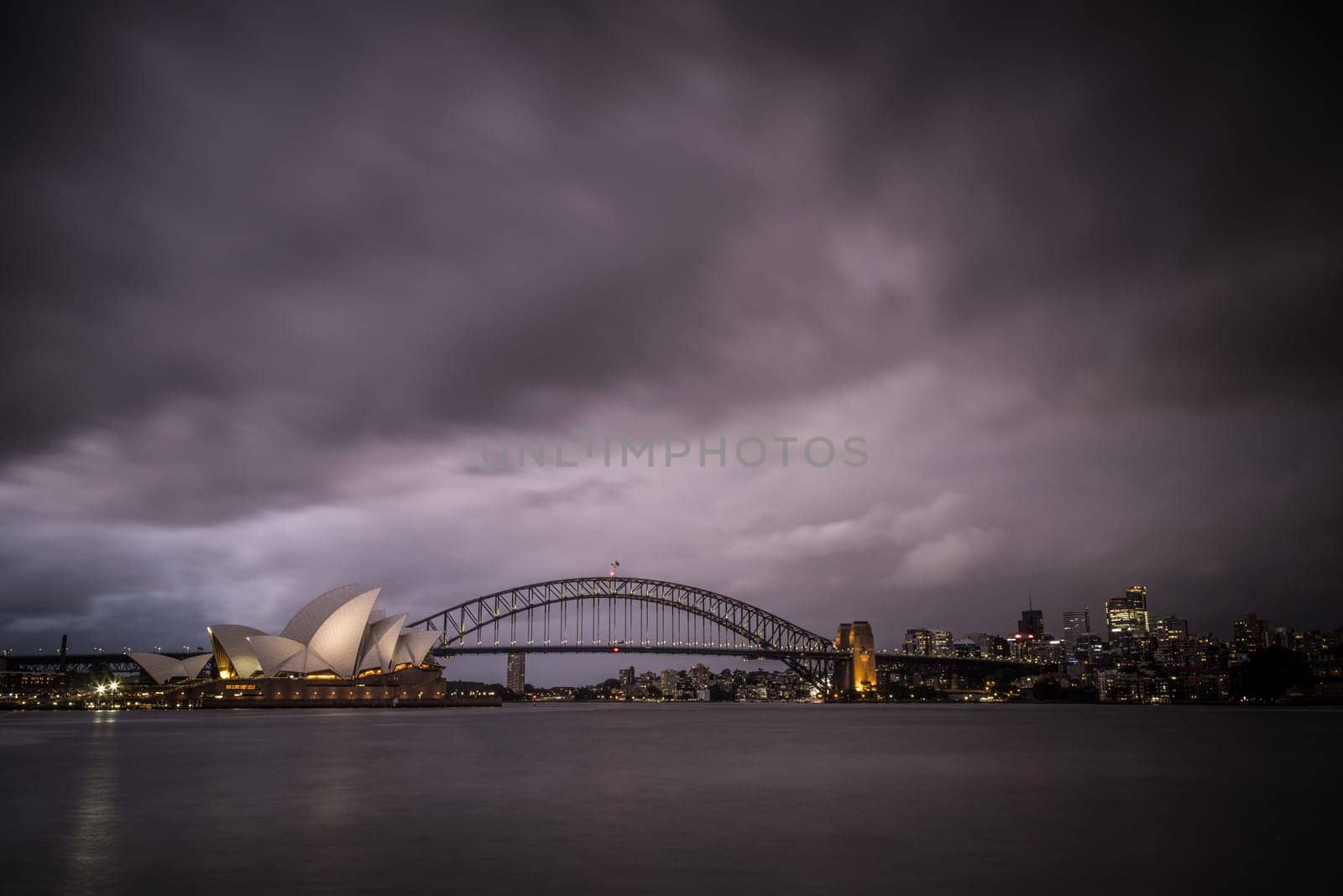 SYDNEY, AUSTRALIA - DECEMBER 03 2023: Sydney Opera House and Harbour Bridge at dusk during a summer storm from Mrs Macquarie's Chair in Sydney, New South Wales, Australia
