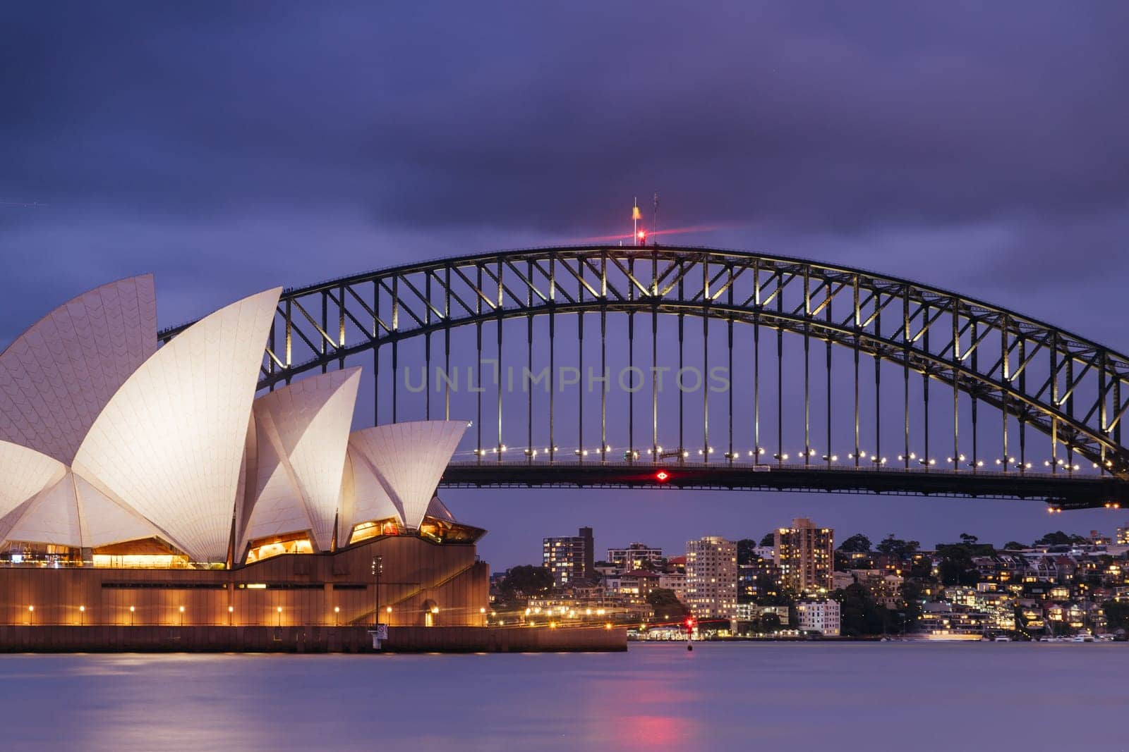 SYDNEY, AUSTRALIA - DECEMBER 03 2023: Sydney Opera House and Harbour Bridge at dusk during a summer storm from Mrs Macquarie's Chair in Sydney, New South Wales, Australia