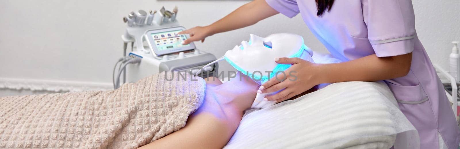woman receiving led light therapy mask treatment from beautician by erstudio