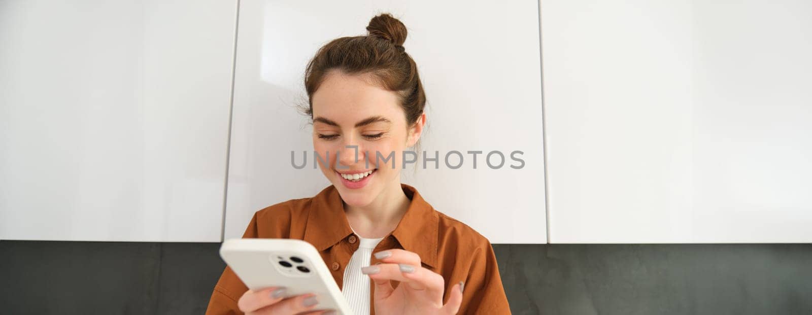 Happy girl with smartphone, looking at phone and smiling, standing at home, concept of buying online, shopping in mobile app.