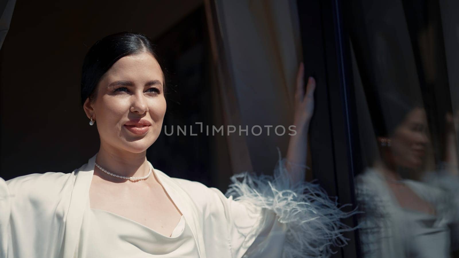 Posing brunette in a sexy white cape. Action. A beautiful woman posing in profile with an open window and the sun. High quality 4k footage