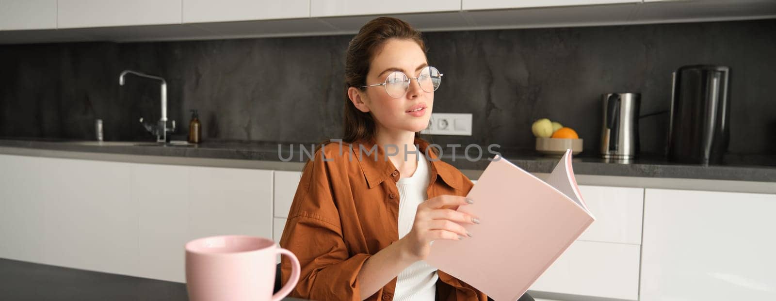 Portrait of woman working from home, sitting in kitchen with documents, opens folder, drinks tea.