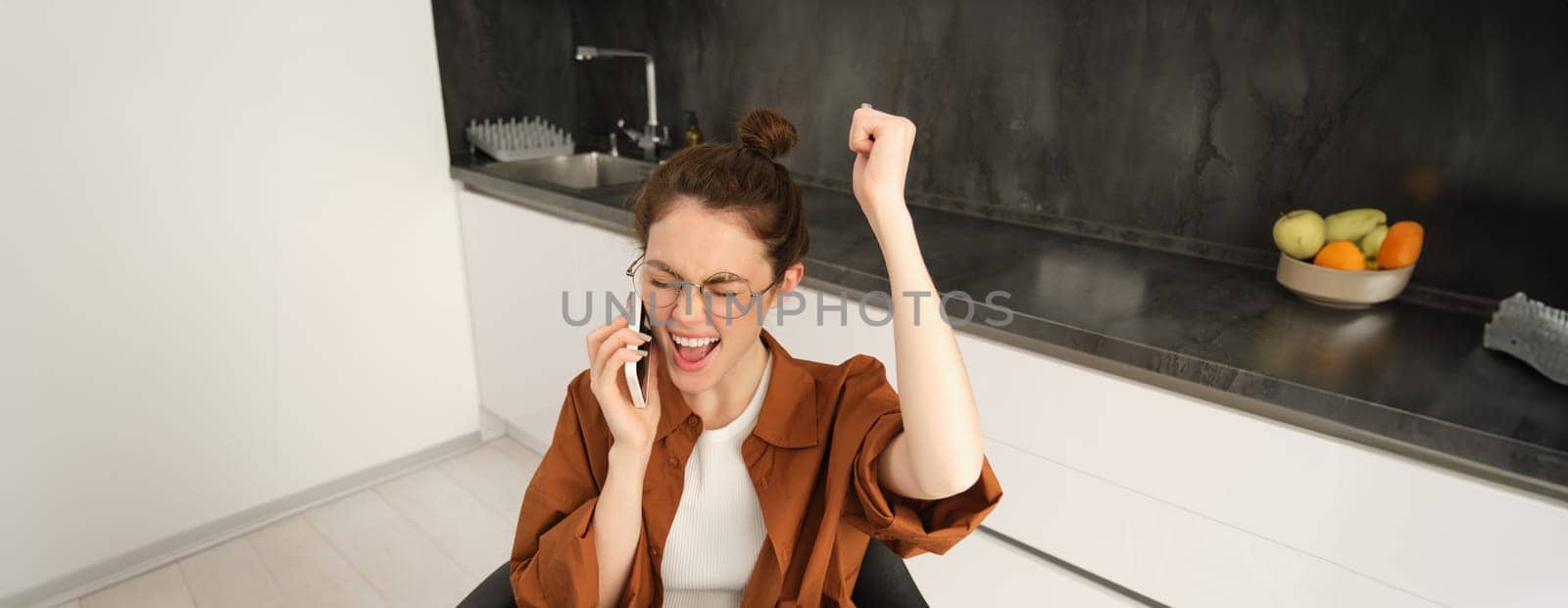 Happy woman receive positive news, job offer over phone call, celebrating, sitting at home, talking on telephone with rejoice, dancing on her seat by Benzoix